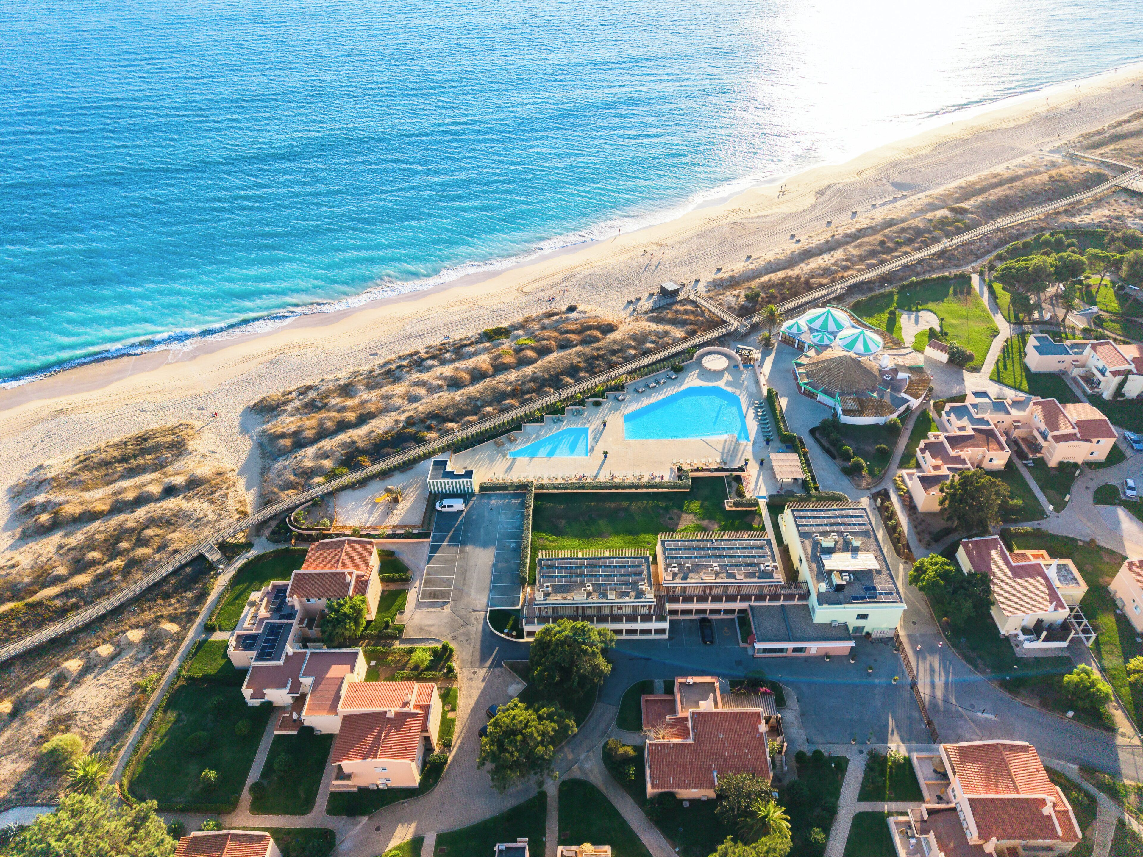 An aerial view of a coastal resort with a swimming pool, beach access, and residential buildings.