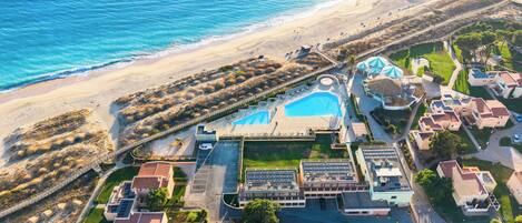 An aerial view of a coastal resort with a swimming pool, beach access, and residential buildings.