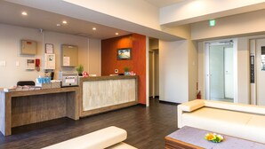 A reception area with a wooden reception desk, a white sofa, and a small table with flowers. - Mr.KINJO in SAKAEMACHI (Naha)