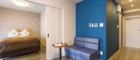 Una habitación de hotel moderna con una cama, una pared azul como acento decorativo, una pequeña mesa redonda y piso de madera.