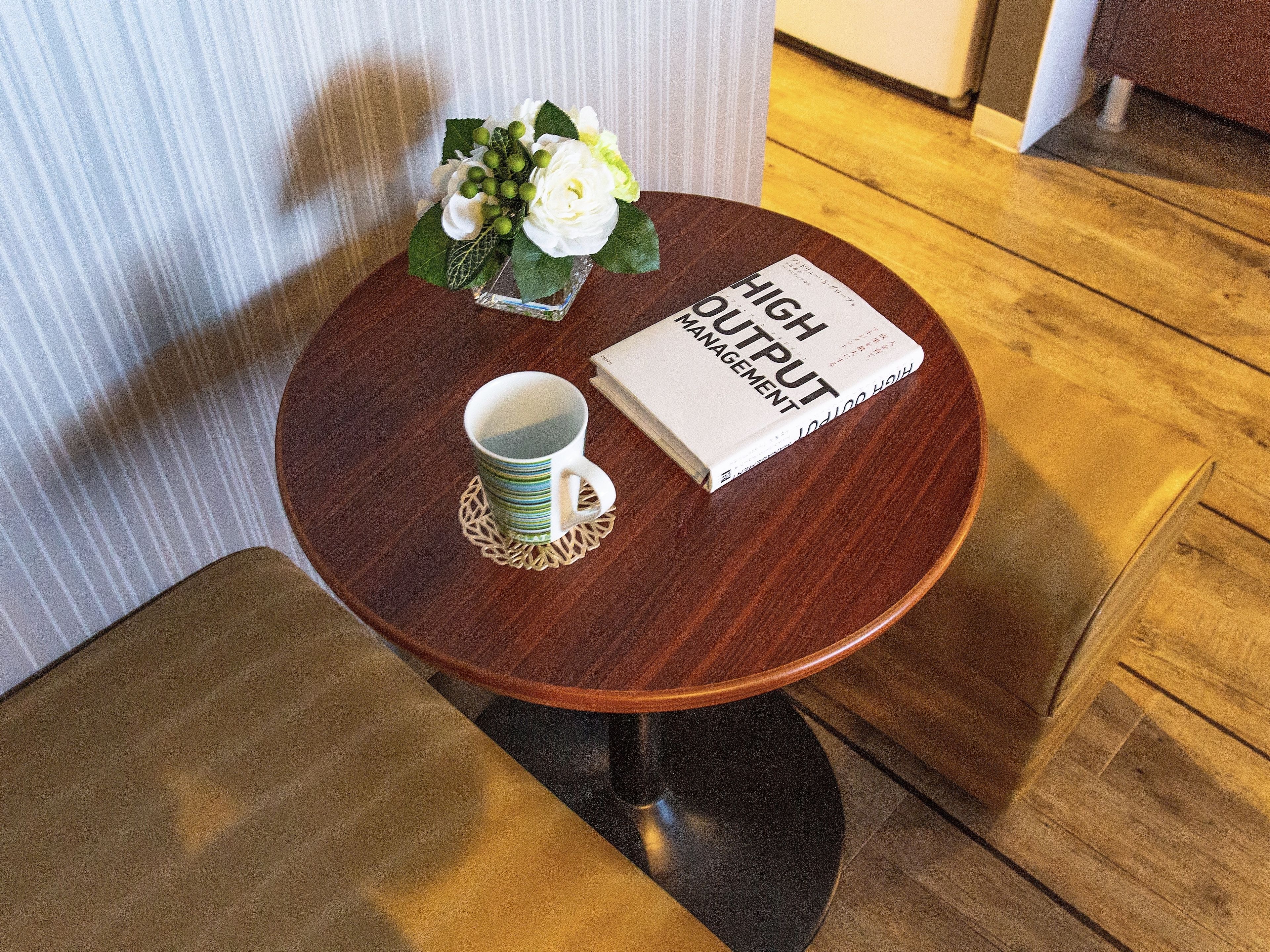 A small round table with a book titled 'HIGH OUTPUT MANAGEMENT' and a cup on a coaster.