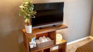 Un meuble en bois pour la télévision, sur lequel est posée une télévision à écran plat, ainsi qu’un pot de plante et des paniers de rangement.
