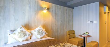 A hotel room with a large bed, a small armchair, a side table with a vase, and a wall-mounted light.