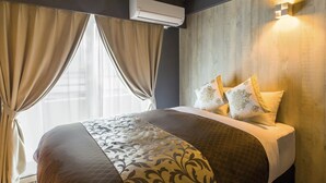 Une chambre d’hôtel avec un grand lit, des rideaux beiges, un appareil de climatisation et un luminaire fixé au mur.