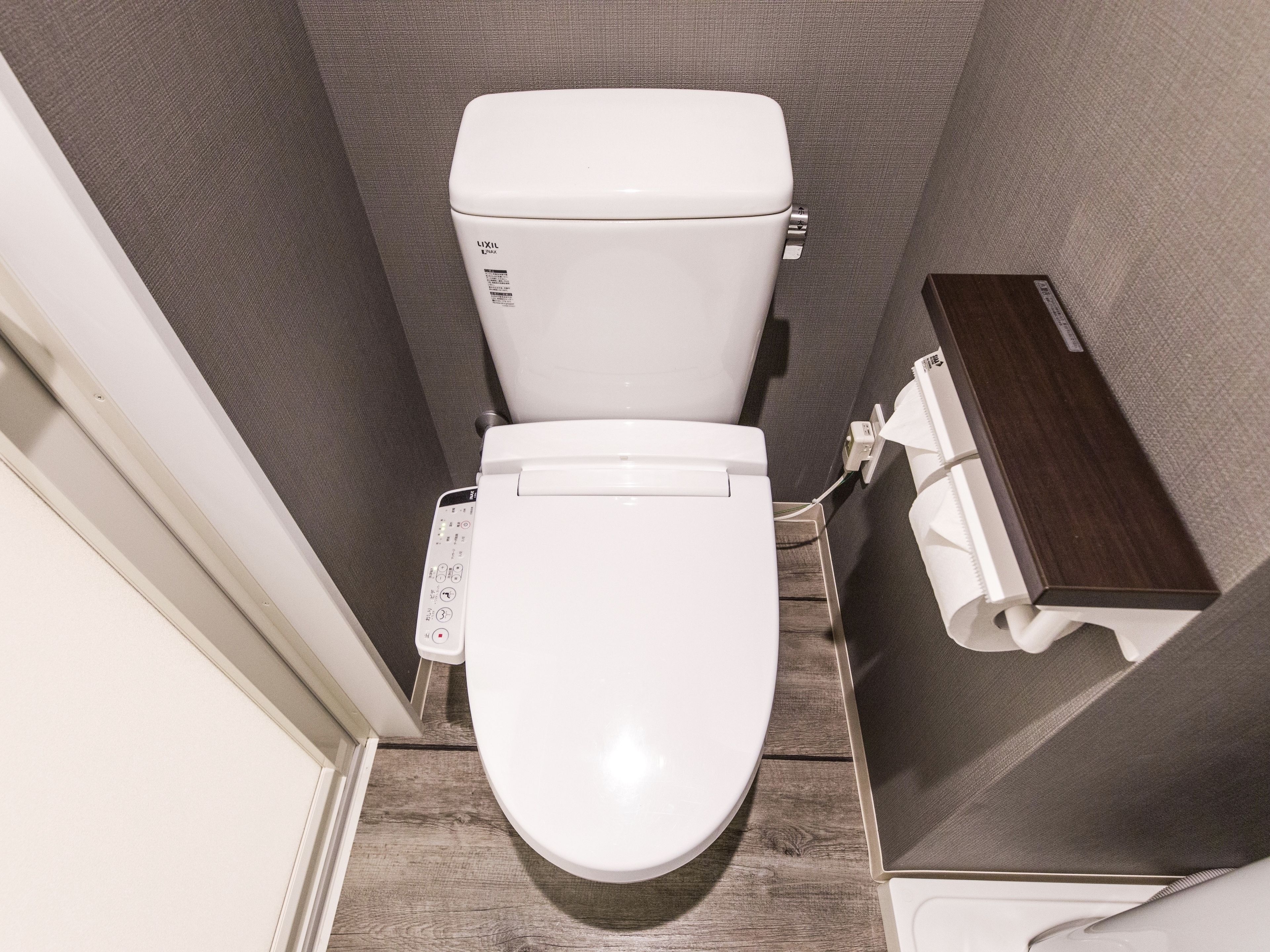 A compact bathroom with a white toilet, a small wooden side table, and a towel dispenser.