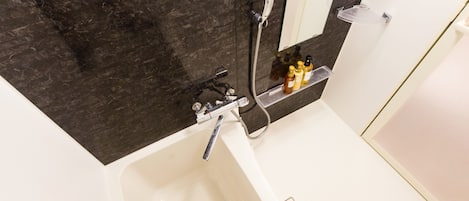 A bathroom with a white bathtub, a dark marble wall, a handheld showerhead, and a shelf with toiletries.