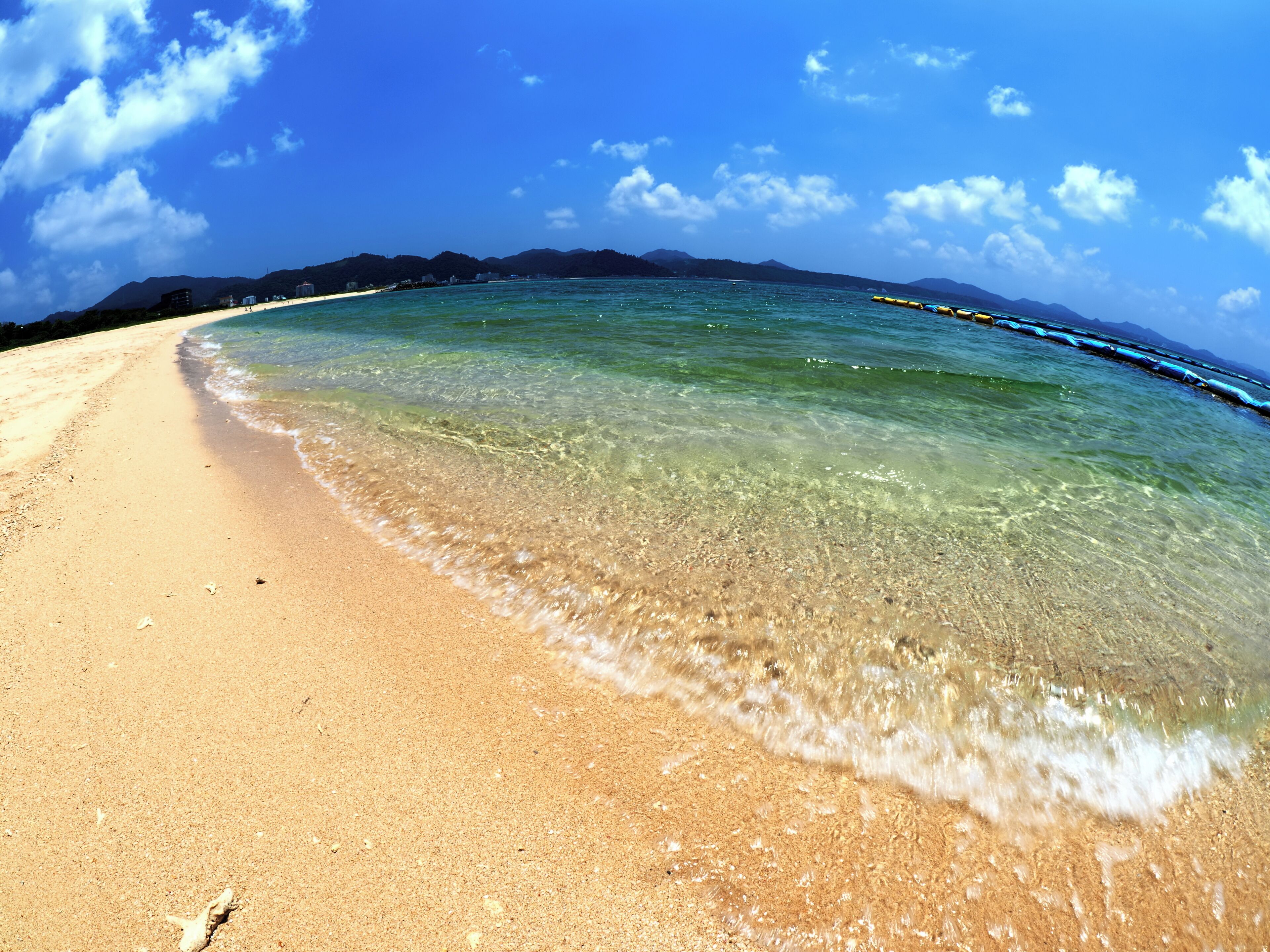 A beach with clear water, a sandy shore, and distant mountains.