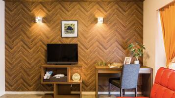 Un salon moderne avec un mur en bois à motifs en chevrons, un téléviseur à écran plat, un meuble de rangement en bois, un bureau avec une chaise et un canapé orange vif.