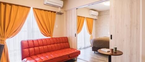 A modern hotel room with a red leather sofa, wooden flooring, and orange curtains.
