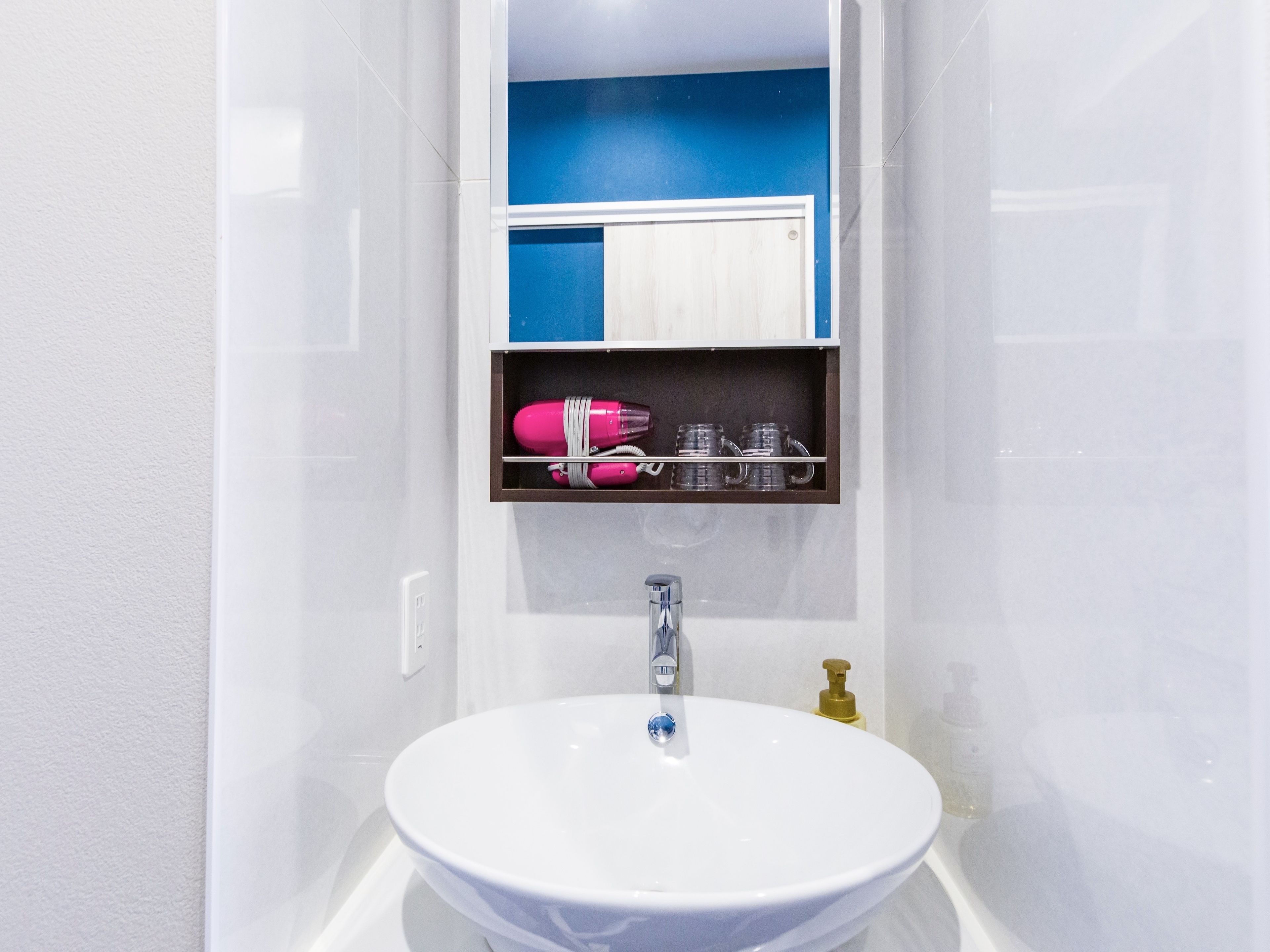 Een badkamer met een wit wastafel, een spiegel en een plankje met een roze haardroger en brillen.