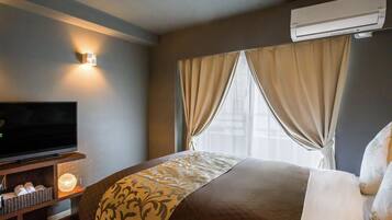 A hotel room with a bed, a television on a wooden stand, and an air conditioning unit.
