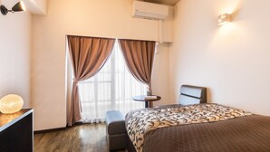 Ein Hotelzimmer mit Bett, Schreibtisch, Stuhl, kleinem Tisch und einem Fenster mit Vorhängen.