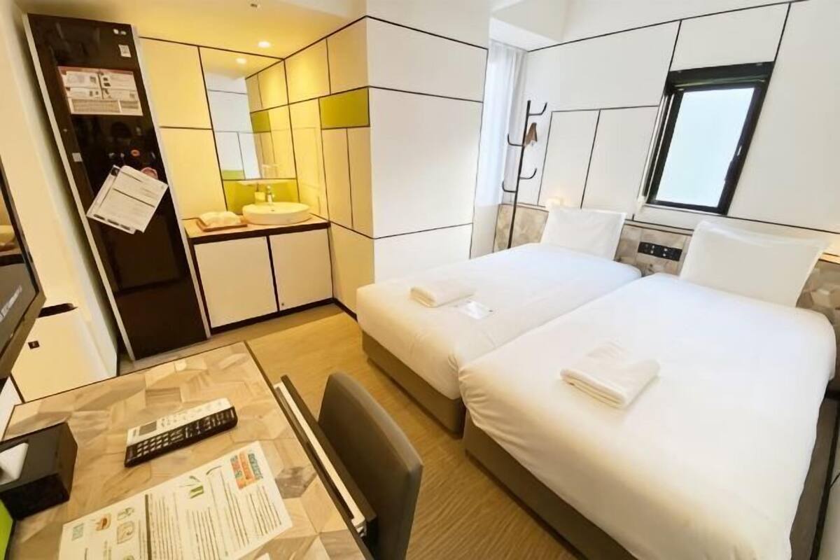 Une chambre d’hôtel avec un lit, un bureau, une chaise, un miroir et une fenêtre.