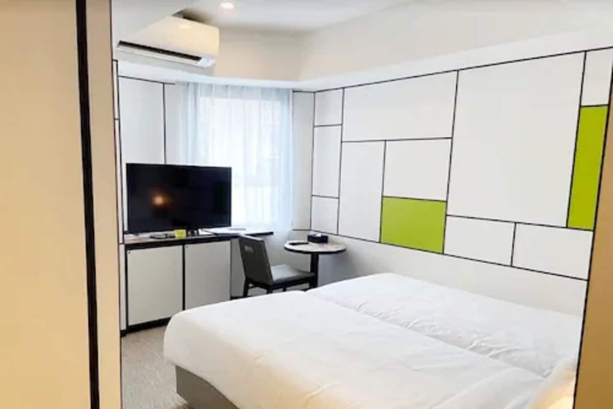 Une chambre d’hôtel moderne équipée d’un lit, d’un bureau avec une chaise, d’une télévision et d’une petite table.