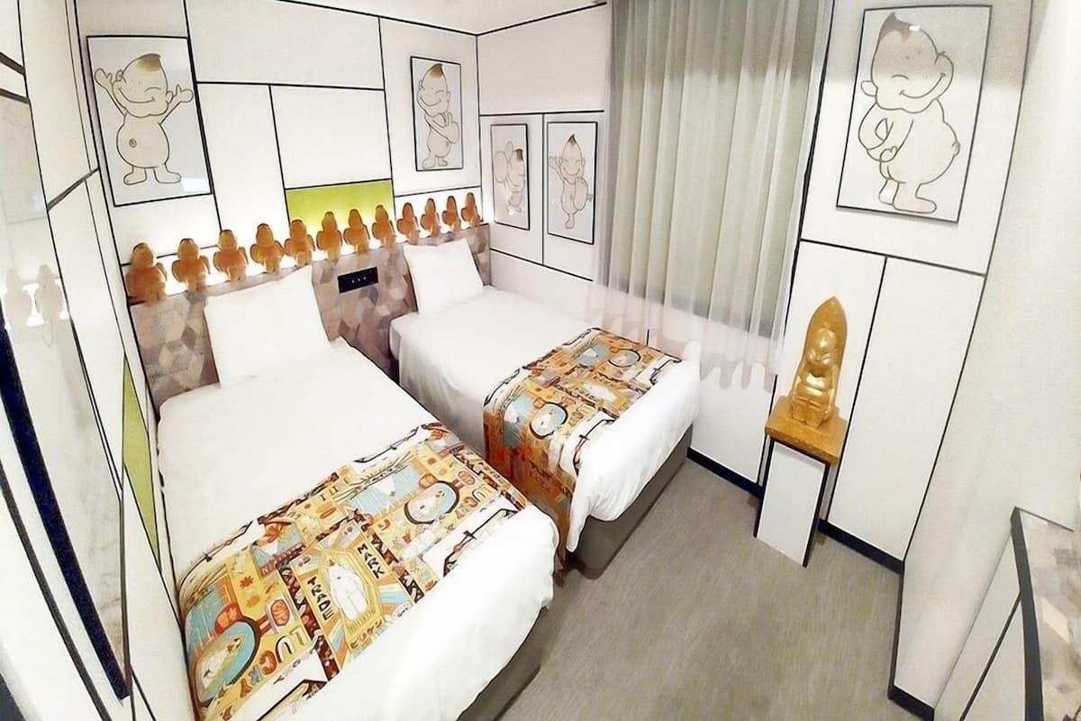 Une chambre d’hôtel avec deux lits, une petite table et des œuvres d’art accrochées aux murs.