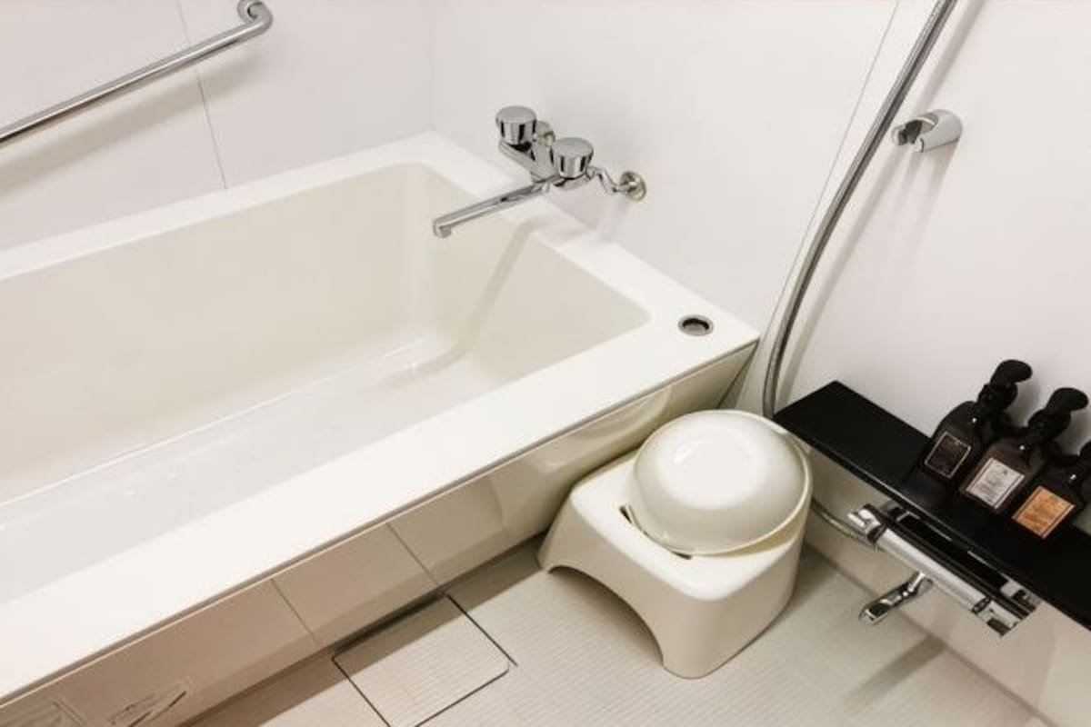 Een witte badkuip met een handdouche, een wit toilet en een zwart wastafel met zeepdispensers.