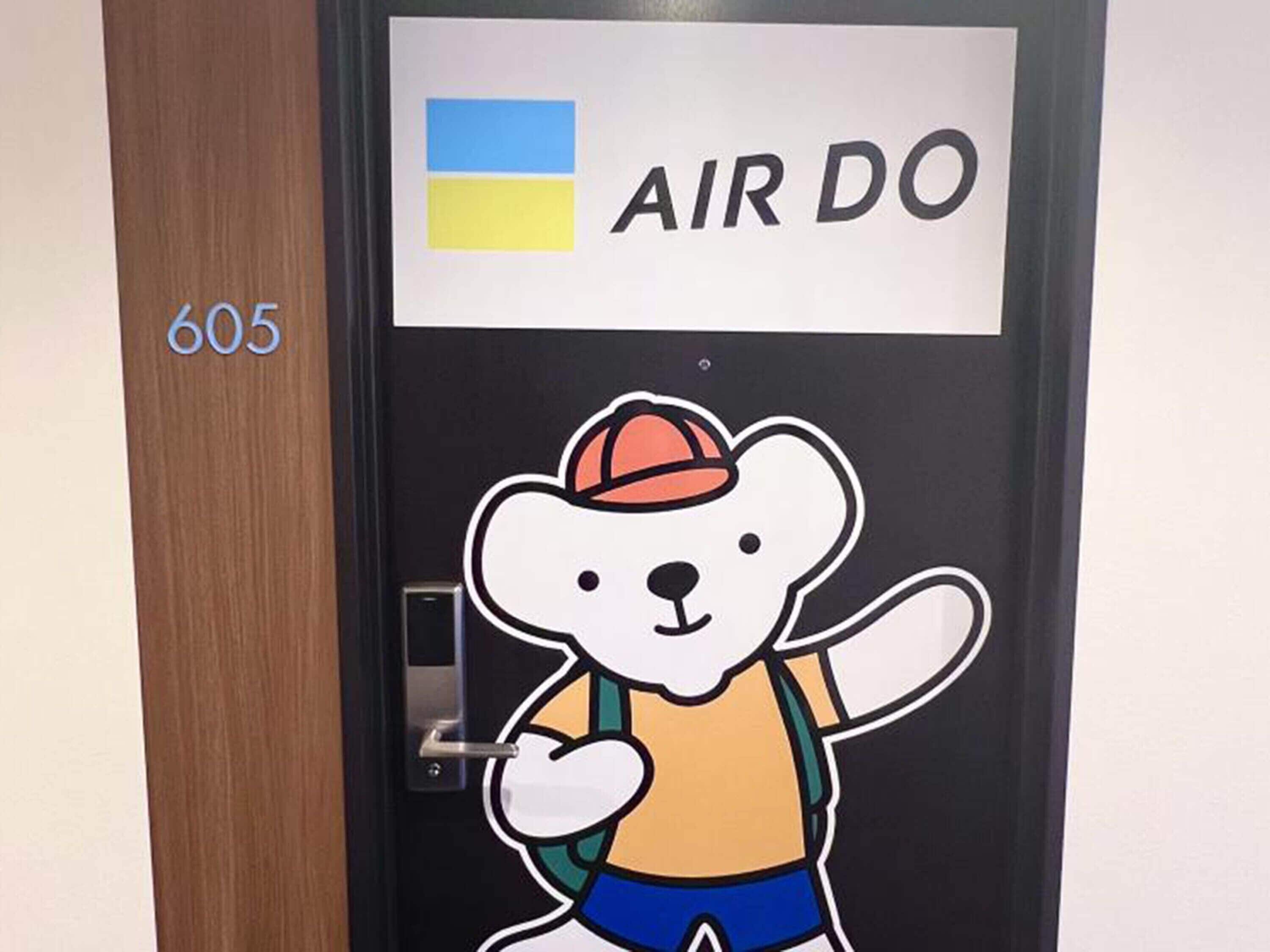 A door with a sticker of a bear wearing a hat and a backpack, and the text 'AIR DO' above it.