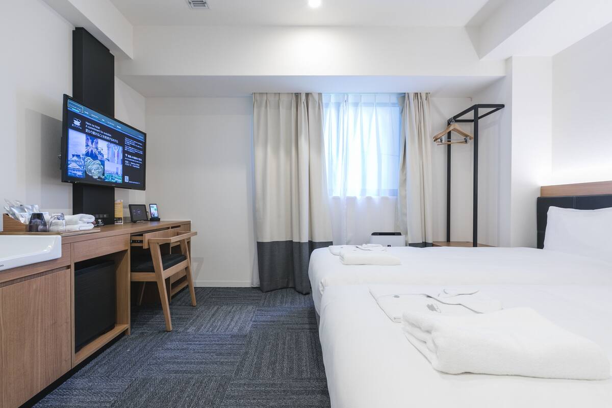 Una habitación de hotel con una cama, un escritorio con computadora, un televisor y un armario.