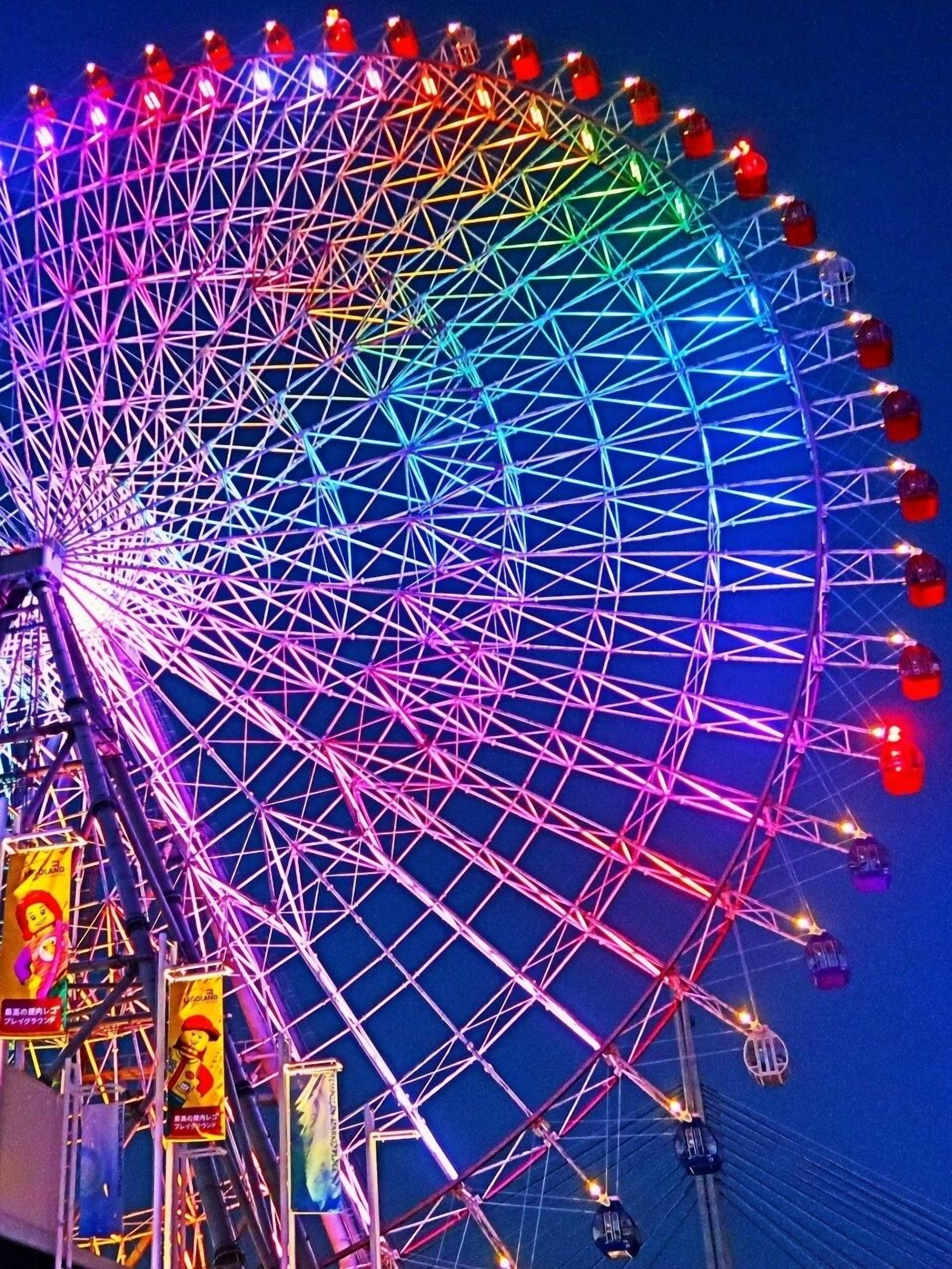 A large Ferris wheel with multiple cabins, illuminated by colorful lights against a dark sky.