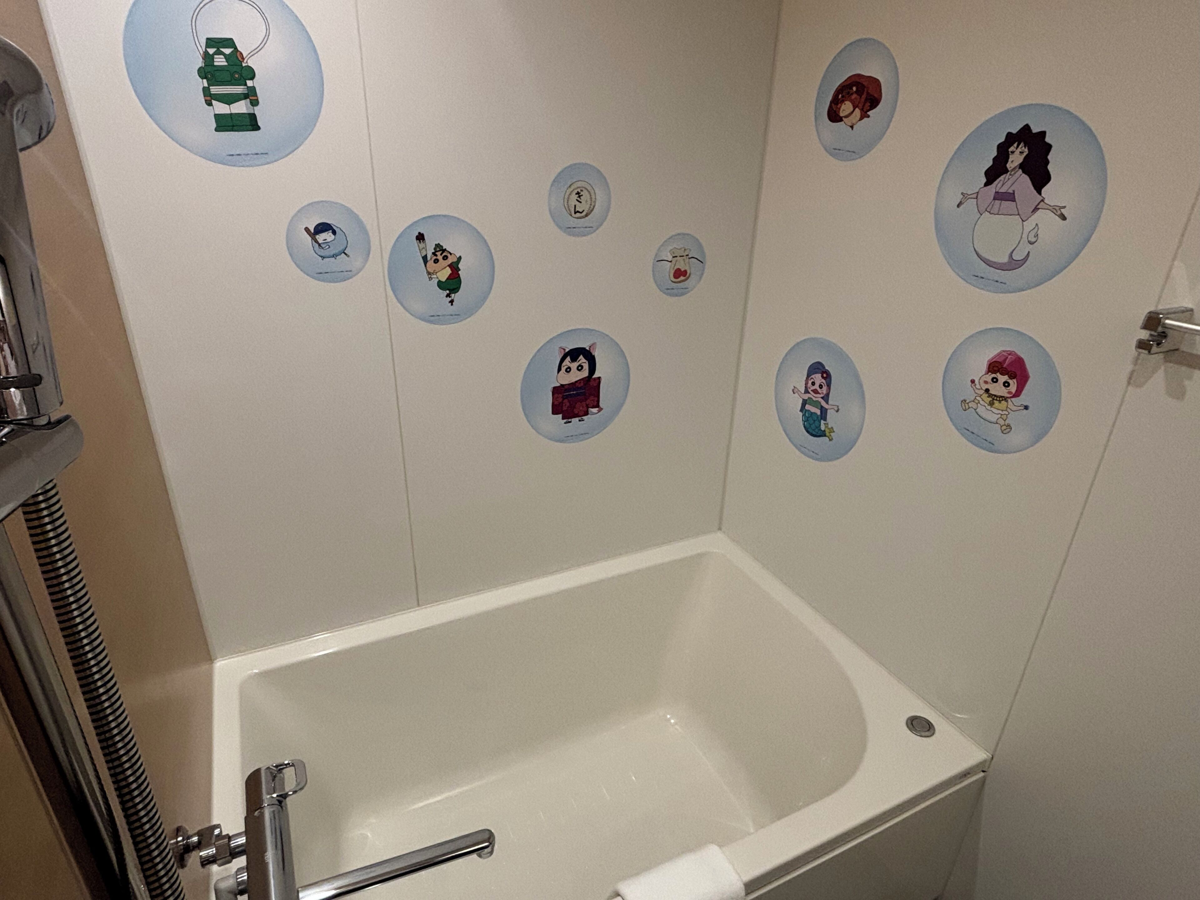 A bathroom with a bathtub, a shower, and a toilet. There are wall stickers with various characters.