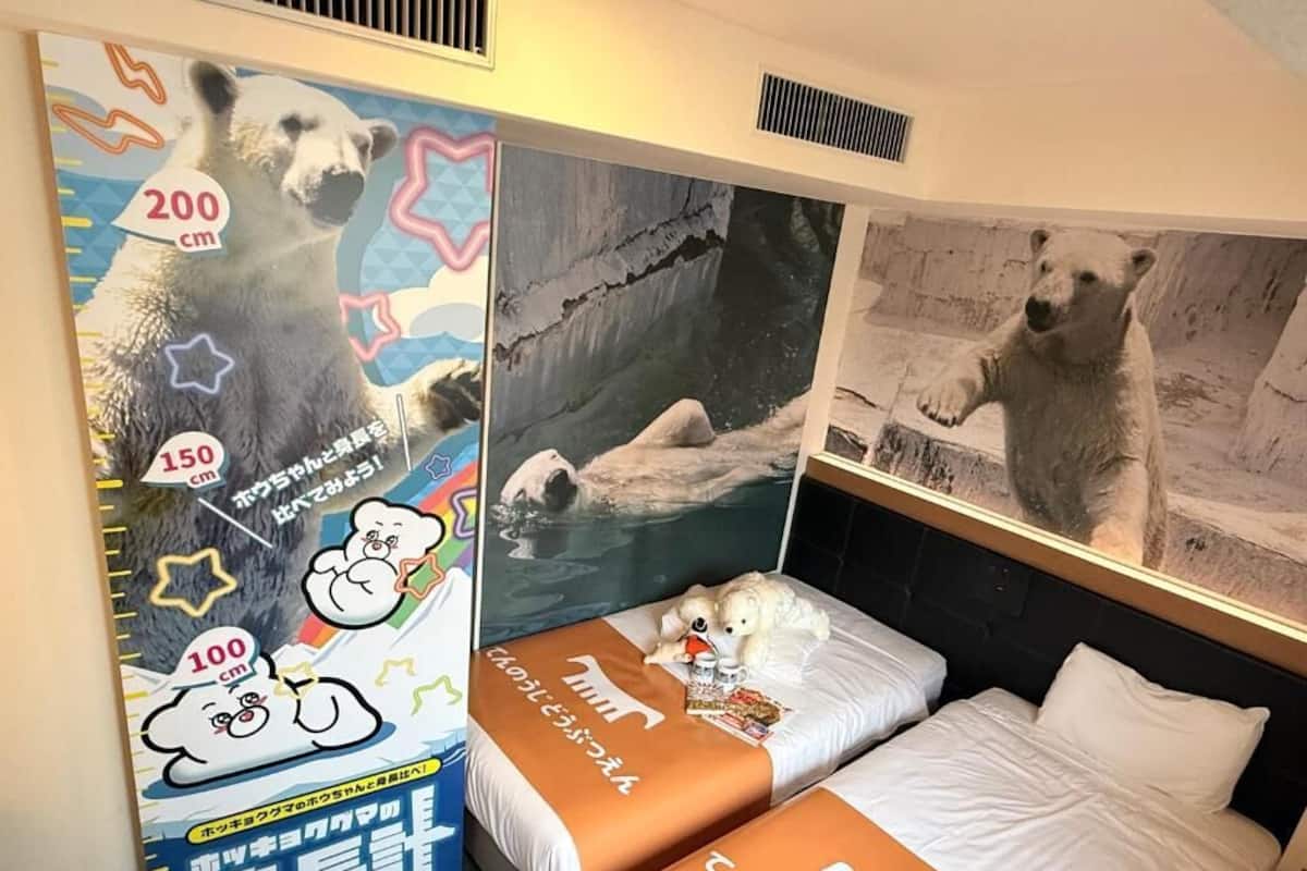 Habitación de hotel con dos camas, un dibujo de un oso polar en la pared y un libro infantil sobre la cama.