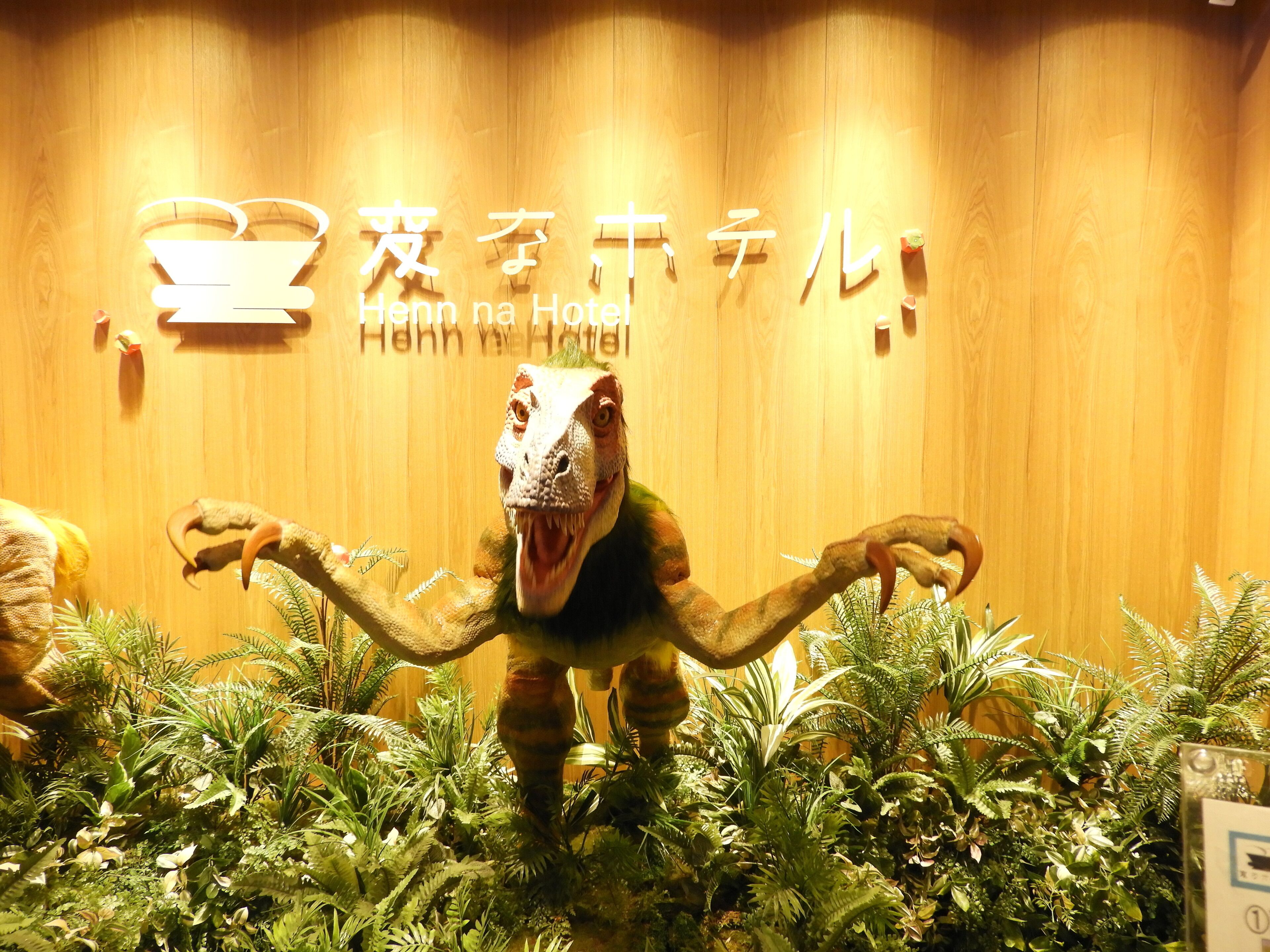 A dinosaur statue in front of a wooden wall with the text "Henn na Hotel".