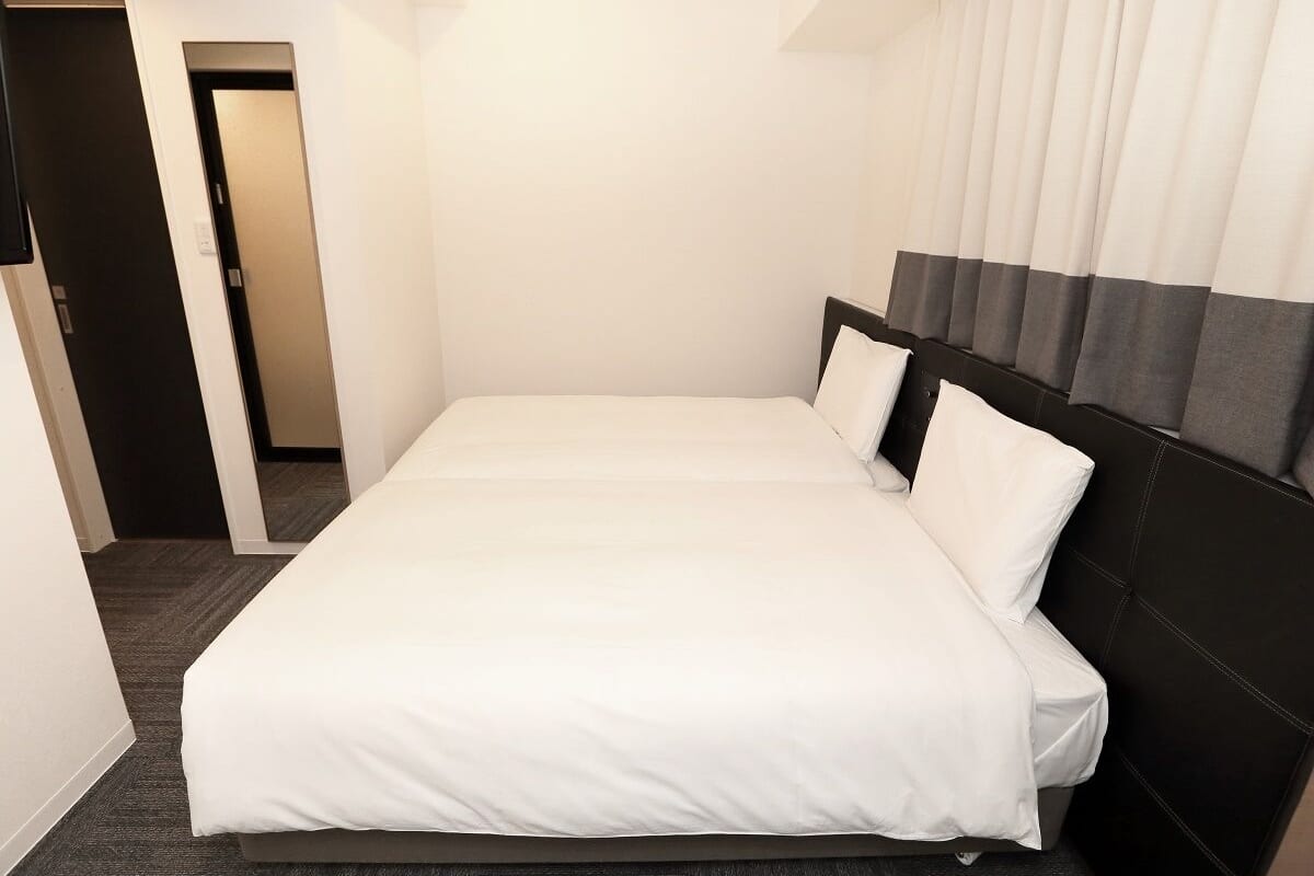 Una habitación de hotel con una cama grande, un cabecero oscuro y suelo alfombrado.