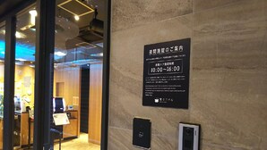 Een bord met openingstijden in Japanse tekst, een beveiligingscodeklavier en een rookmelder aan een muur.