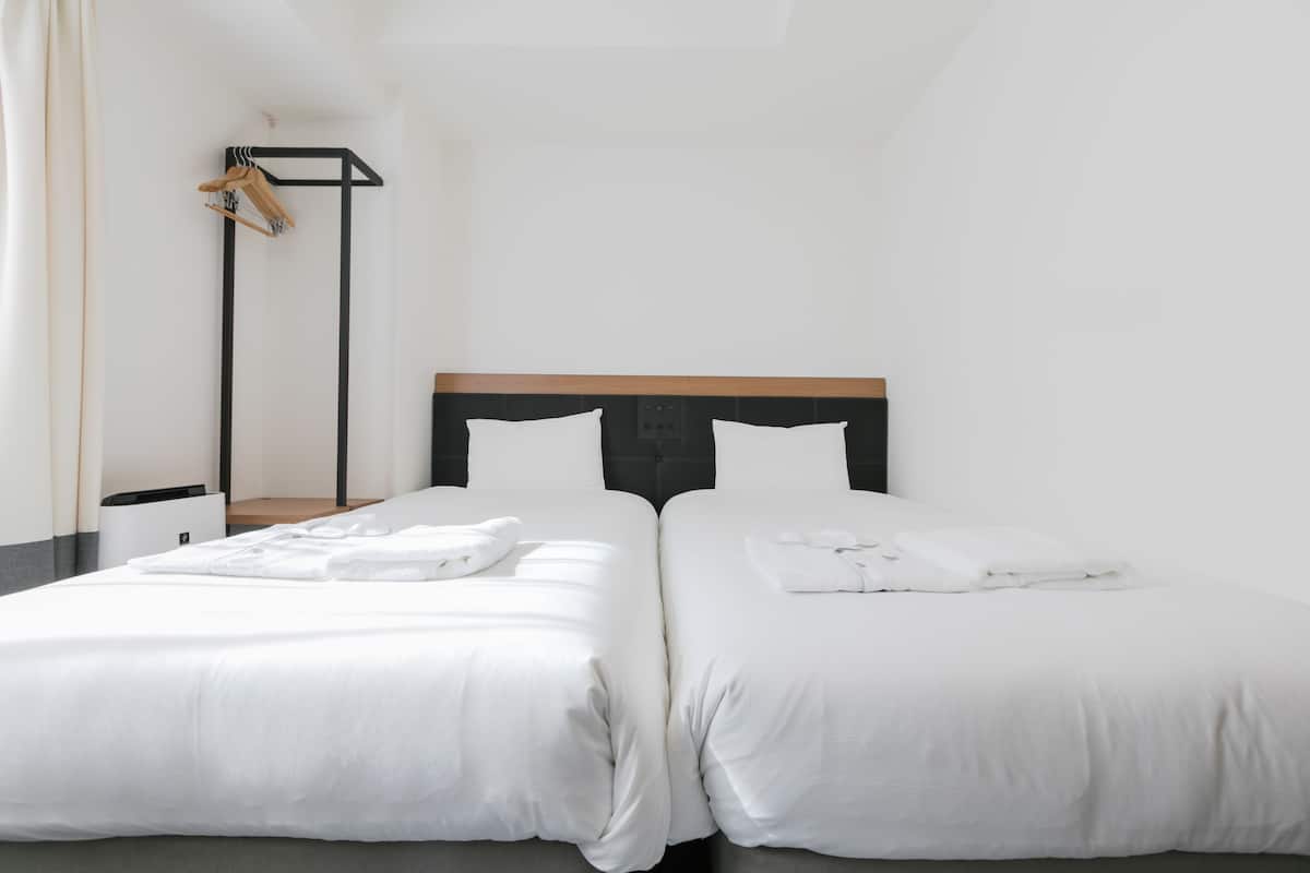 Habitación de hotel con dos camas, cabecero de madera y una mesita de noche con lámpara.