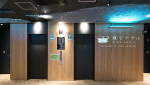 Een hotel receptie met houten lambrisering, een lift en een bord dat bezoekers welkom heet in Henn na Hotel.