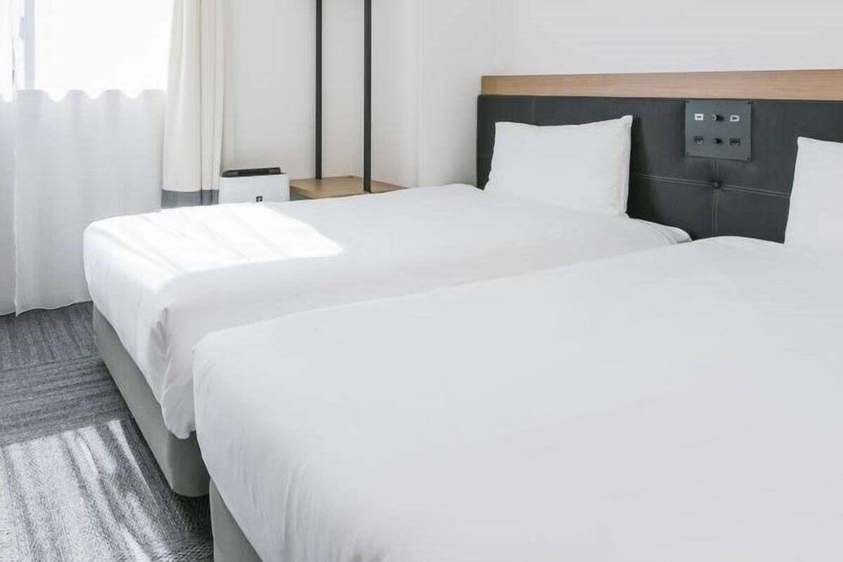 Habitación de hotel con dos camas, una mesita de noche y un panel de control en la pared.