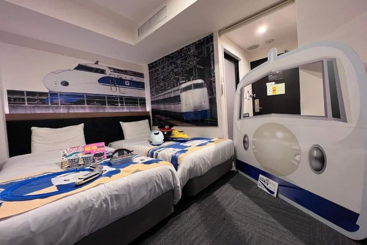 Habitación de hotel con dos camas, un ventanal grande y un mural en la pared con un tren.