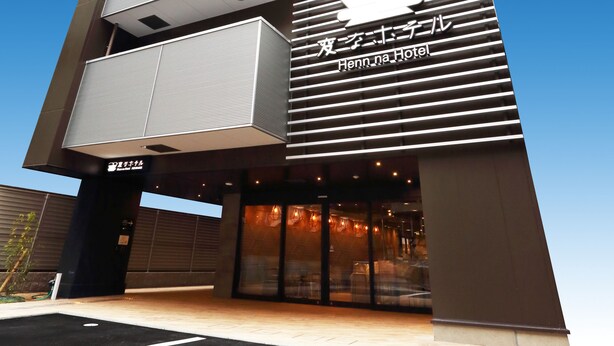 Een modern hotel met een opvallend logo, meerdere balkons en een heldere lucht.