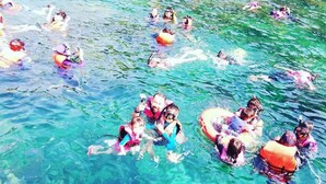 A group of people swimming in a clear blue body of water, likely a pool or lake, with some wearing life jackets. - Juara Mutiara Resort (Tioman Island)
