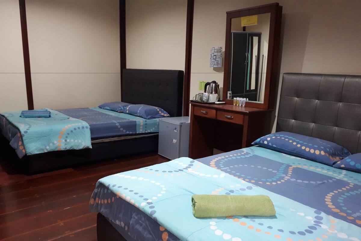 A hotel room with two beds, a small desk, a mirror, and a wardrobe.