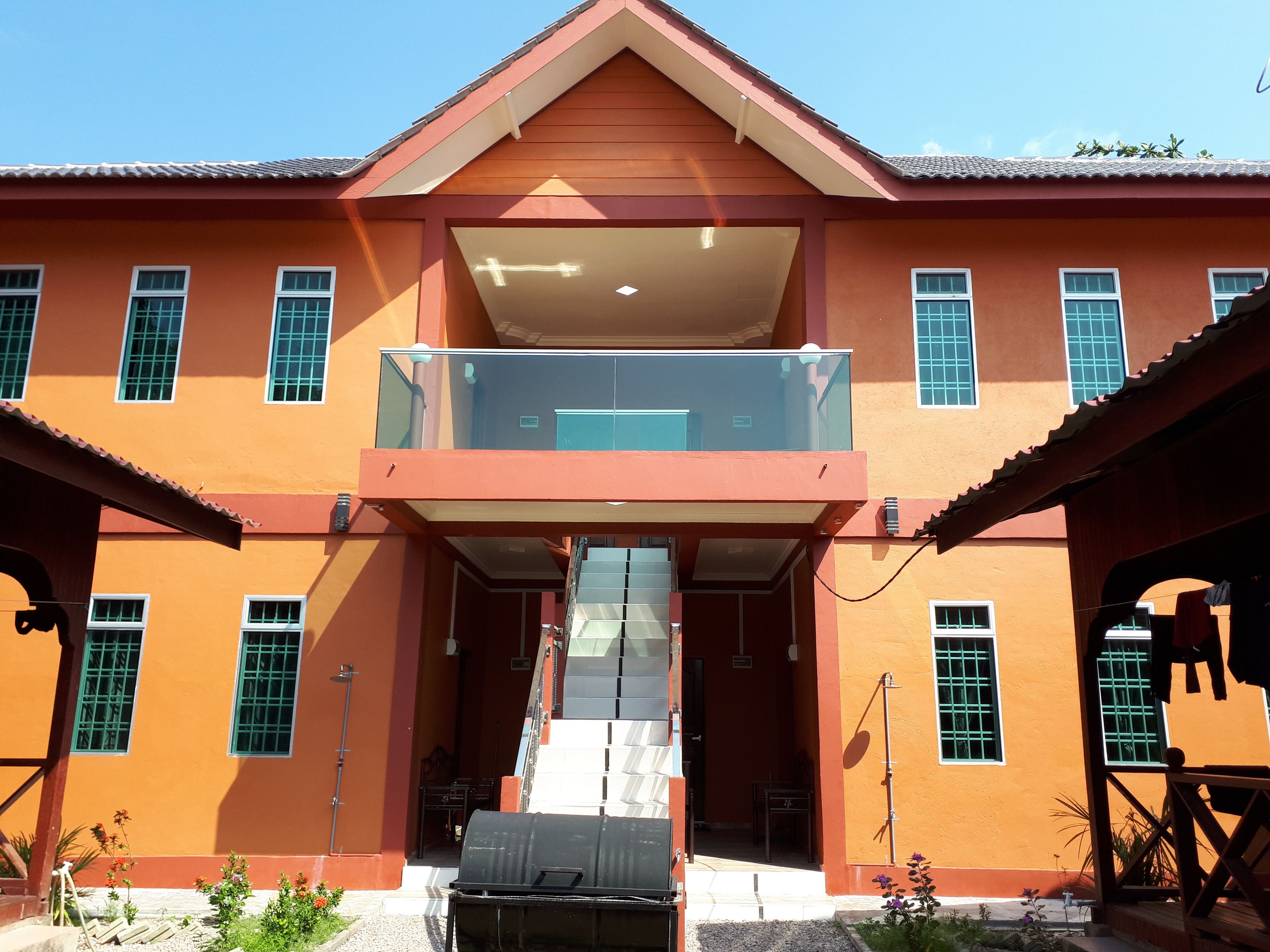 A two-story building with a balcony on the upper floor, a covered entrance, and a small outdoor seating area.