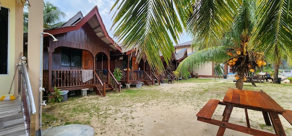 A wooden building with a porch, a palm tree with coconuts, and a wooden table.