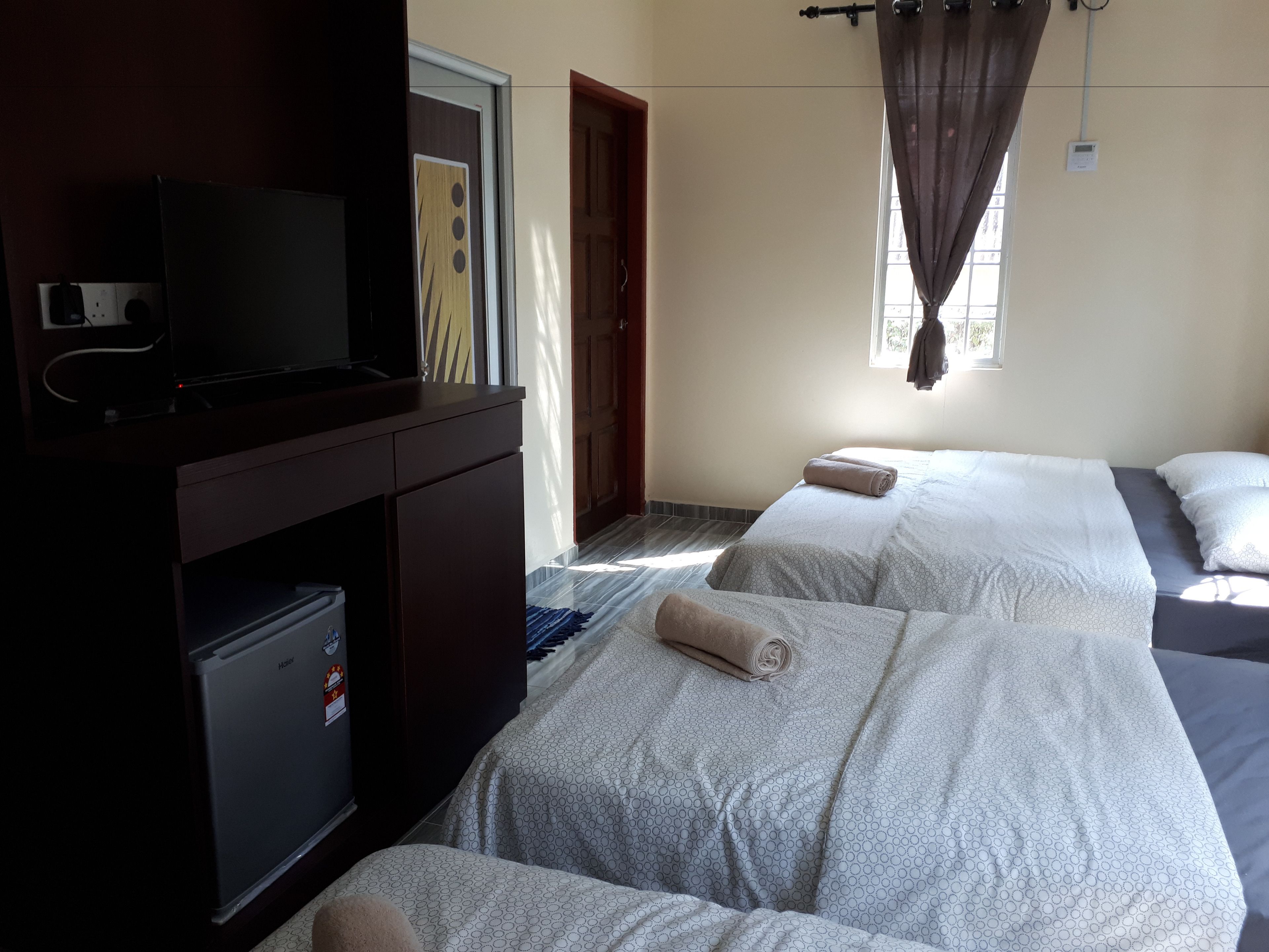 A hotel room with two beds, a TV, a minibar, and a window with curtains.