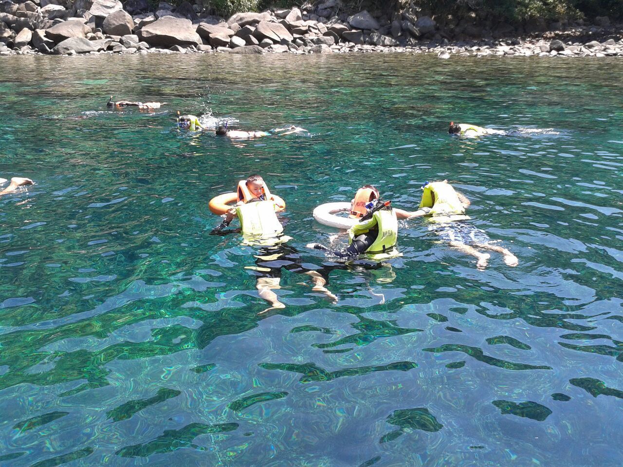 Un grupo de personas nadando en un río claro y rocoso.