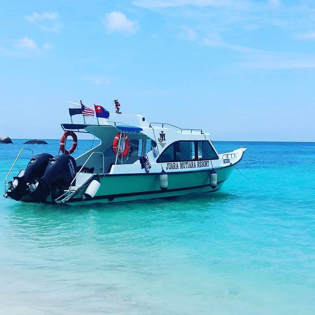 Un barco llamado 'JUARA MUTIARA RESORT' con chalecos salvavidas y una bandera, amarrado en aguas turquesas cristalinas.