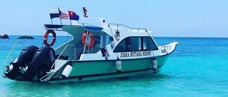 A boat named 'JUARA MUTIARA RESORT' with lifebuoys and a flag, docked in clear turquoise waters.