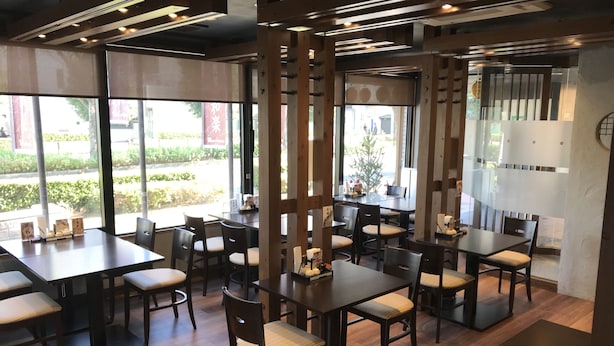 Interior de restaurante con varias mesas y sillas, ventanas amplias y vistas al exterior.