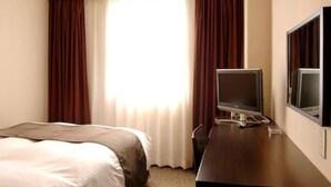 Una habitación de hotel con cama, escritorio con televisor y ventana con cortinas.