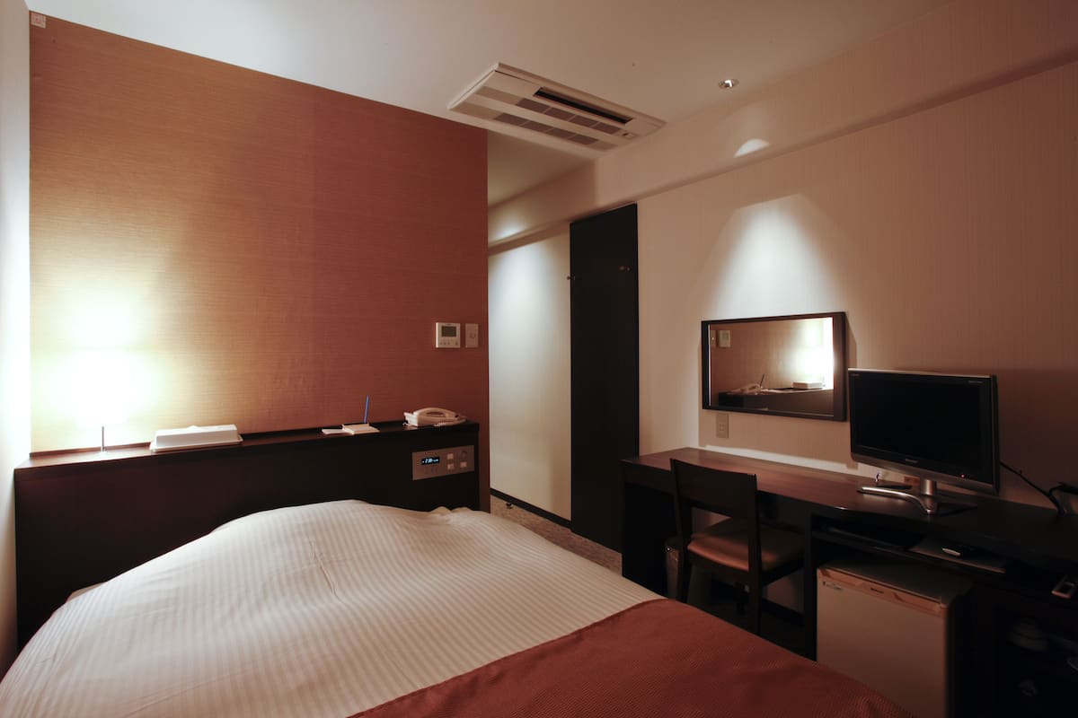 A hotel room with a bed, a desk, a television, and a small refrigerator.