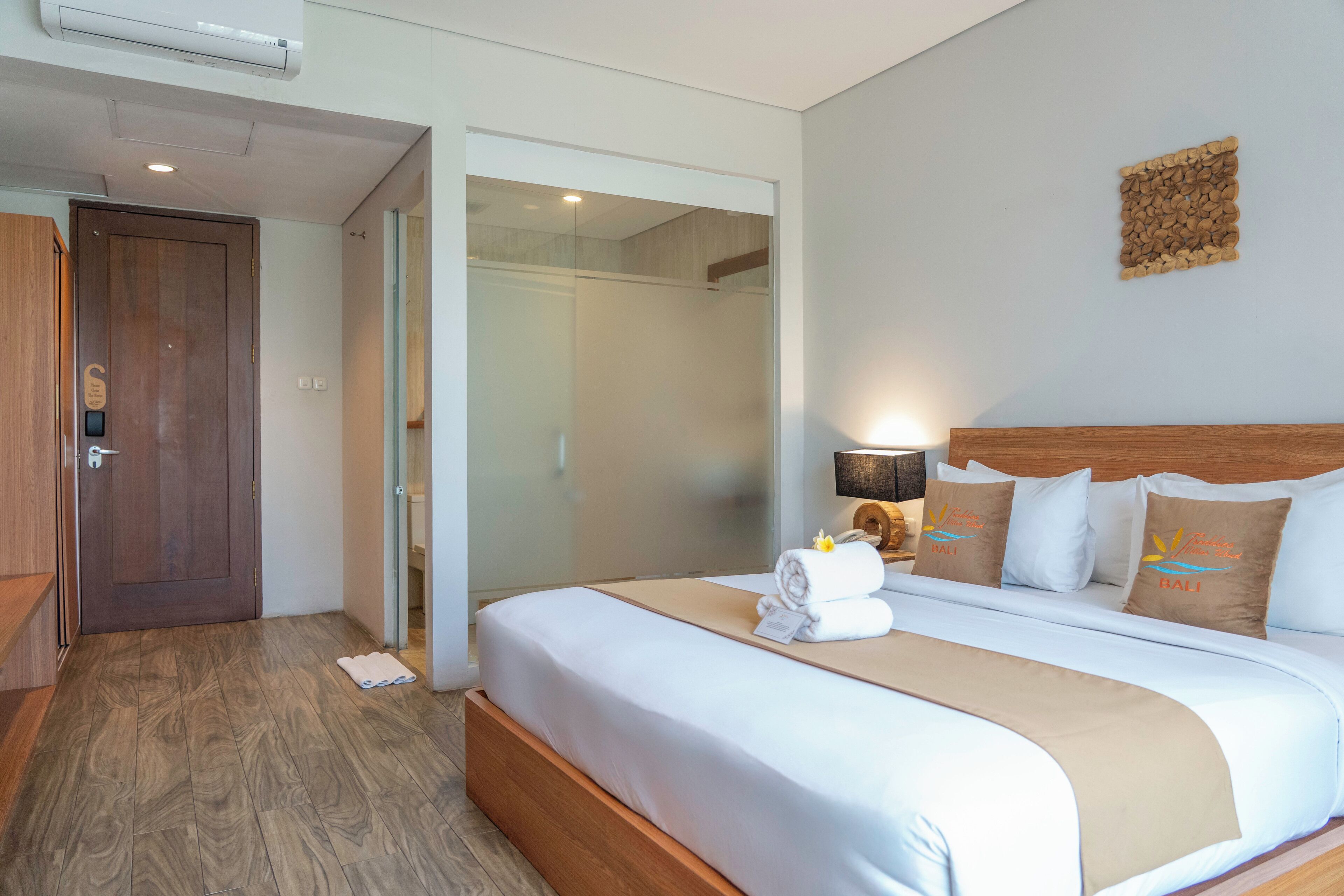 Quarto de hotel com uma cama grande, porta de madeira e divisória de vidro.