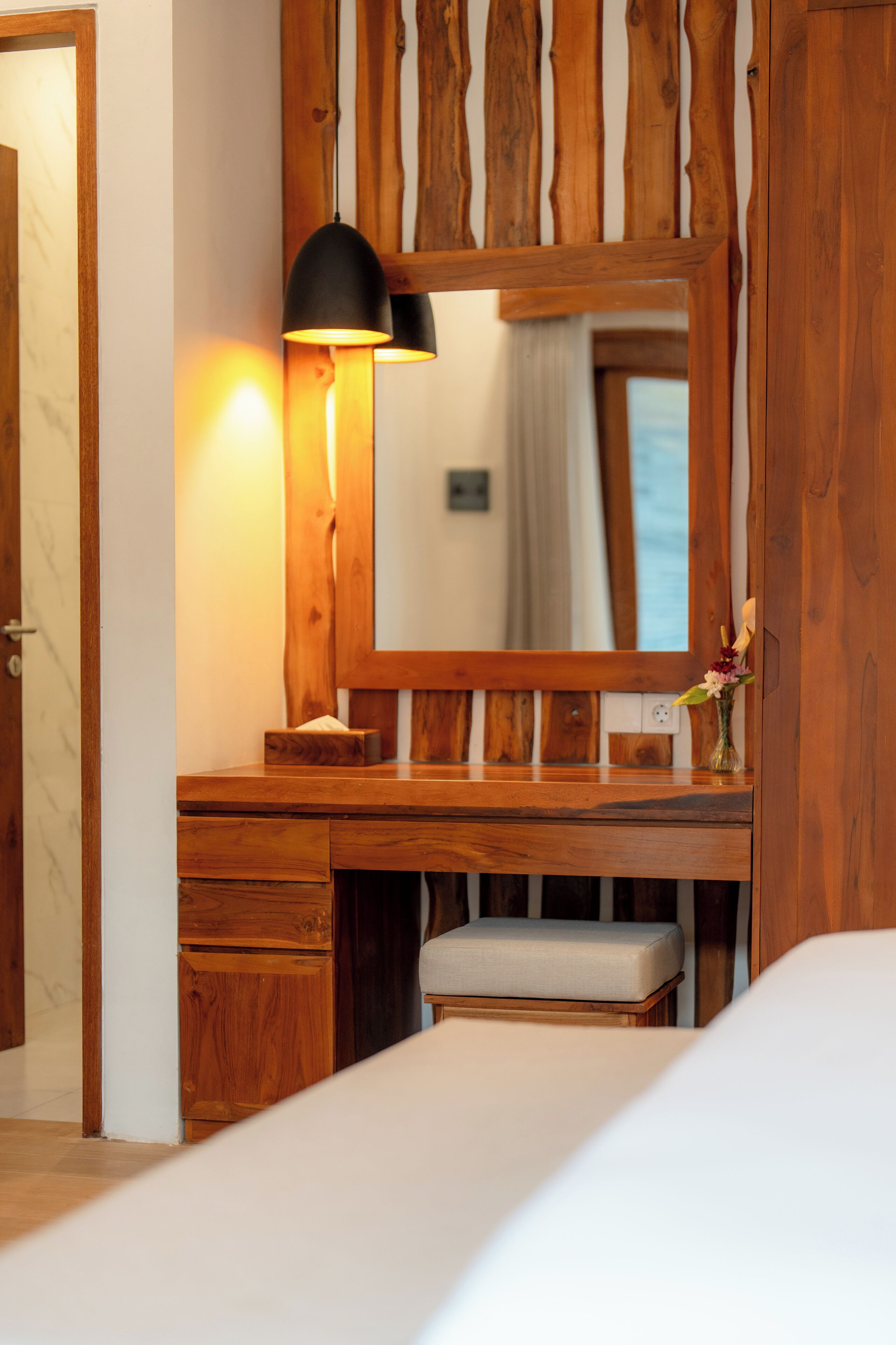 A wooden vanity with a mirror, a lamp, and a vase with flowers.