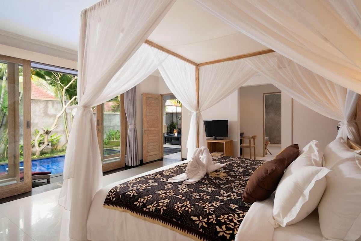 A bedroom with a canopy bed, a television, and a view of the outdoors.