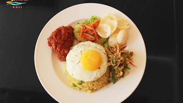 Un plato de comida con un huevo frito, arroz, verduras y una guarnición de sambal y papas fritas.