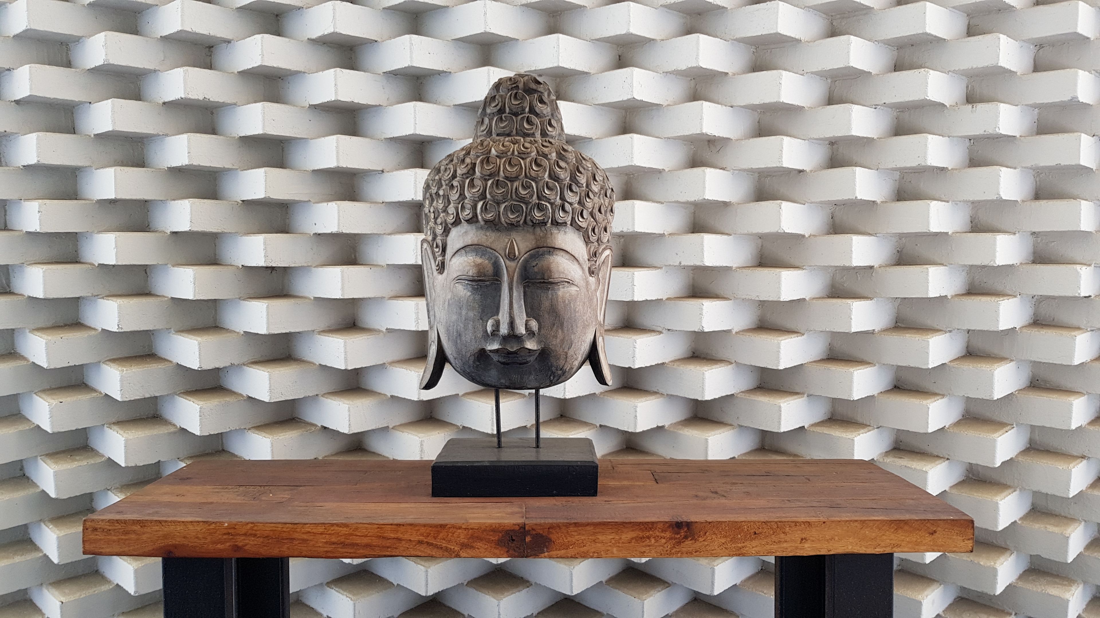 A Buddha head sculpture on a wooden table against a patterned wall.