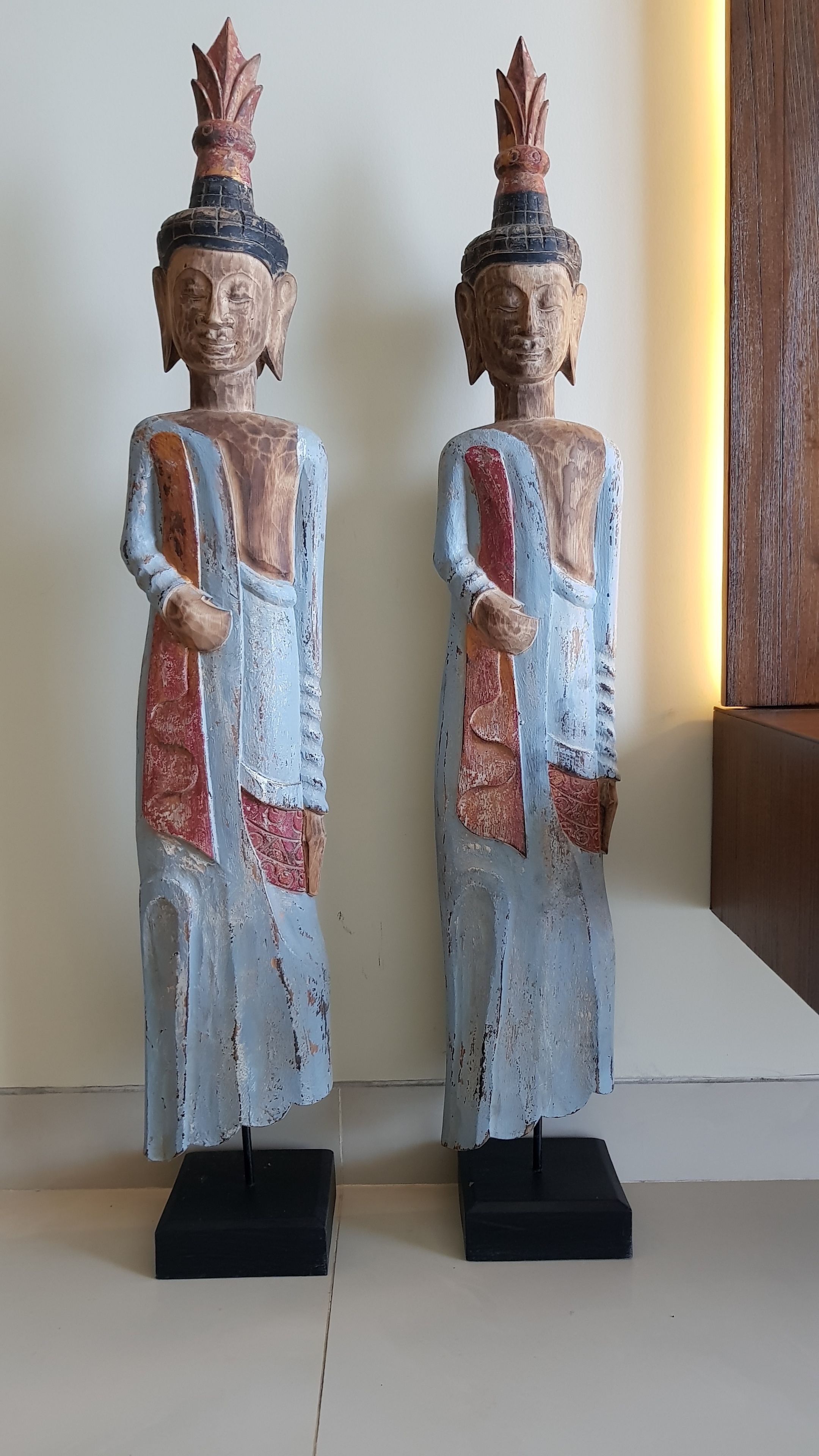 Two wooden statues with a blue and red color scheme, placed on black pedestals.